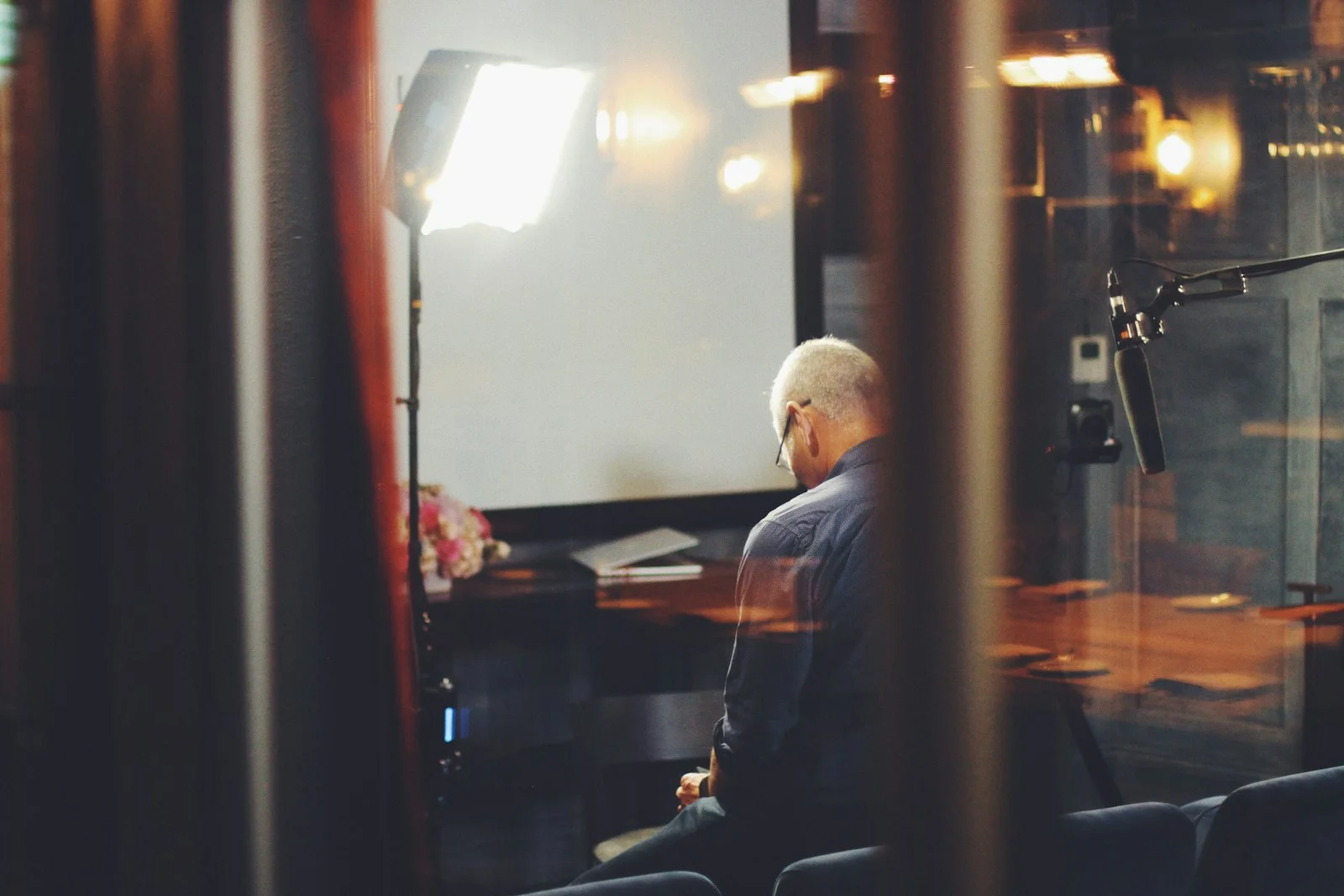 Grey-haired man seated beneath a studio light and boom microphone, preparing for a recorded interview